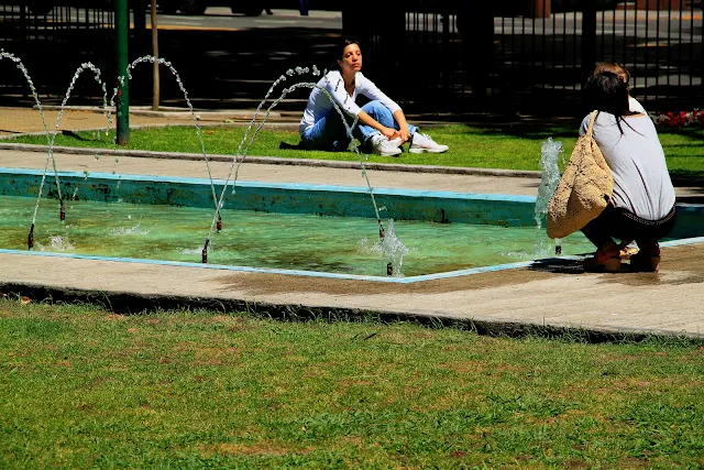 Junto a una fuente de agua dos mujeres hablando