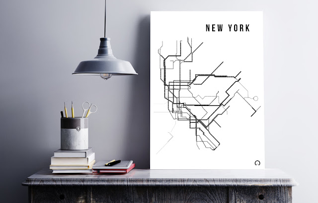 Plakat, grafika projektu Moje Metro z artystycznem przedstawieniem schematycznego planu metra w Nowym Jorku. Czarno-biały obraz stojący na biurku obok książek, ołówków i metalowej lampy.