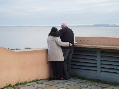 foto de um casal de idosos abraçados admirando o lago Guaíba, na usina do gazômetro, em um dia nublado em porto alegre