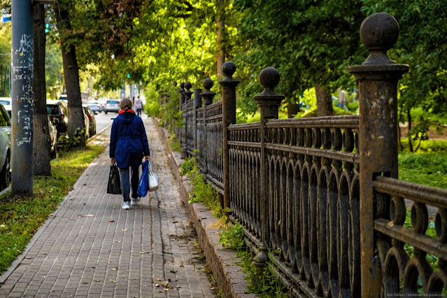 Женщина идет по тропинке вдоль ограждения парка