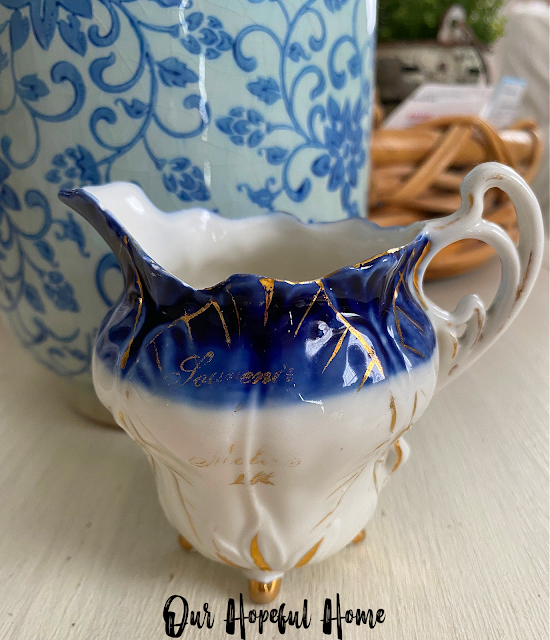 tiny porcelain creamer Souvenir Moline Ill. in front of blue and white vase and round rattan tray