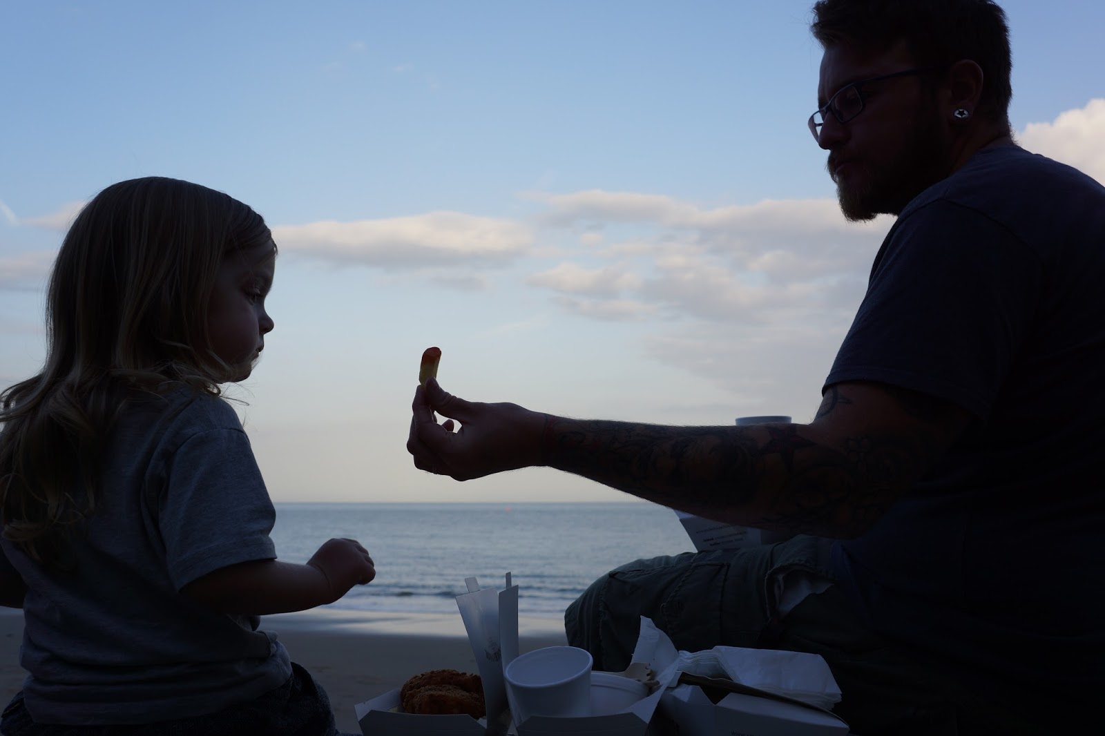 dad eating fish and chips with toddler at the beach in the evening