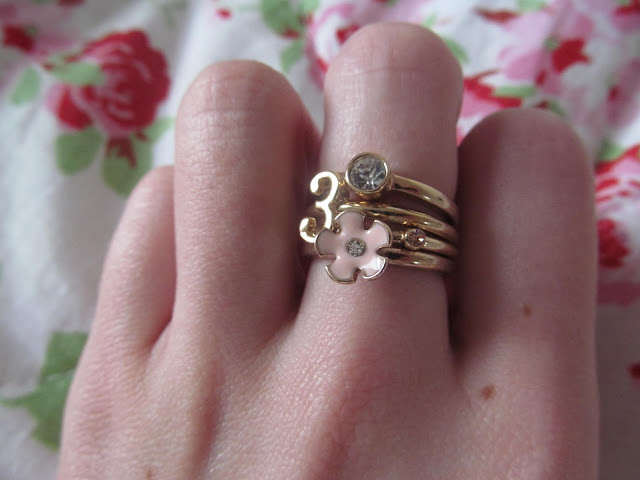 four gold costume rings stacked on middle finger - one with pink flower, two with gemstones and one with the number 3