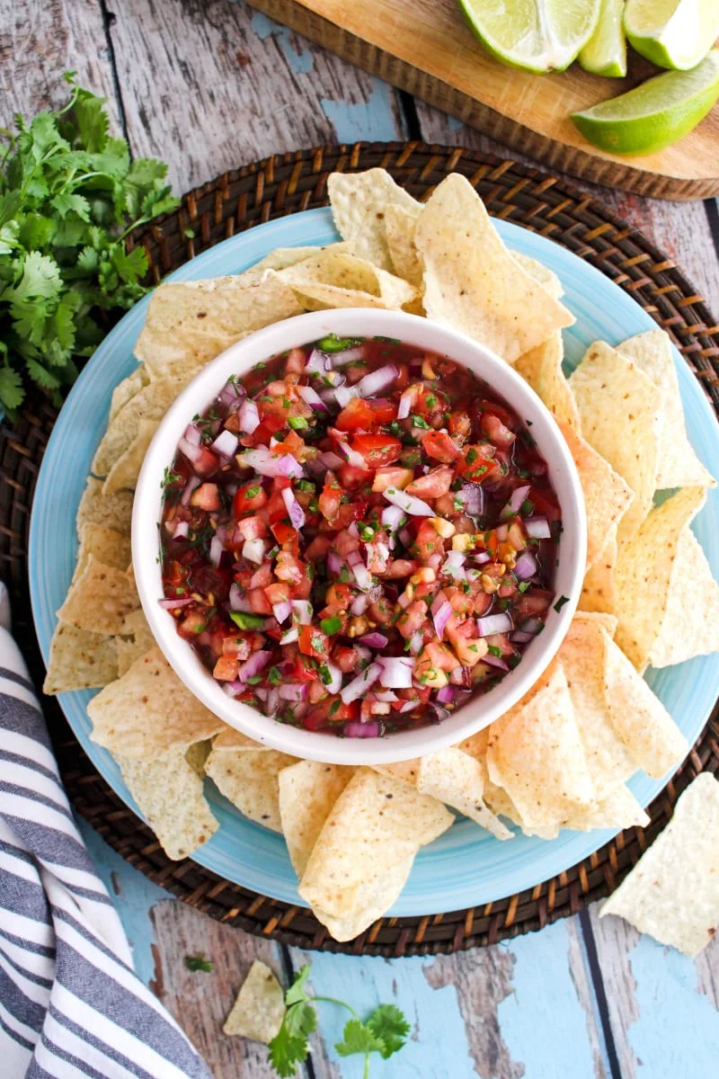 Salsa fresca in a bowl surrounded by tortilla chips on a blue plate.