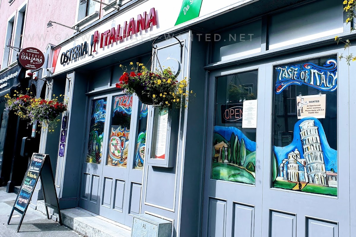 Shopfront in Galway city painted with stereotypical Italian mems including the leaning tower of pizza.   Also hanging baskets of red and yellow flowers.