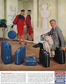 an American Tourister advertisement from 1962 featuring Oleg Cassini, a popular fashion designer of the era, sitting on top of and beside a set of blue and black hard side American Tourister luggage. in the background, a fashionable lady wearing red carries a blue American Tourister hat box