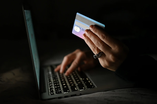 An illustrative image of a person holding a credit card while shopping on-line on a computer