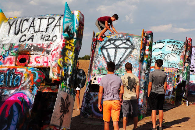 A kid creating some Cadillac Ranch graffiti up on top of one of the Cadillacs.