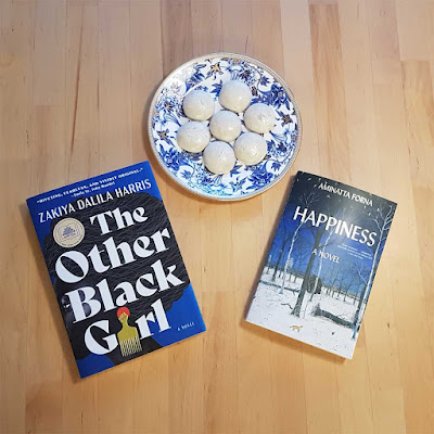 Two books on a table, The Other Black Girl and Happiness, with a pretty blue plate with Pfeffernusse biscuits