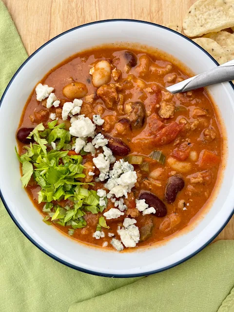 Serving a bowl of Buffalo chicken chili with blue cheese and celery leaves on top.