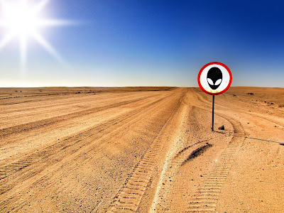 A desert landscape with trails of tire tracks and a sign displaying an alien symbol.