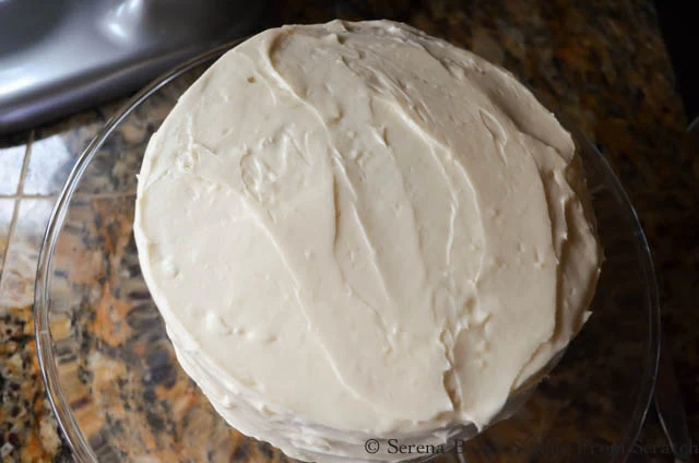 Carrot Cake with Pineapple covered with cream cheese frosting on a glass cake stand.