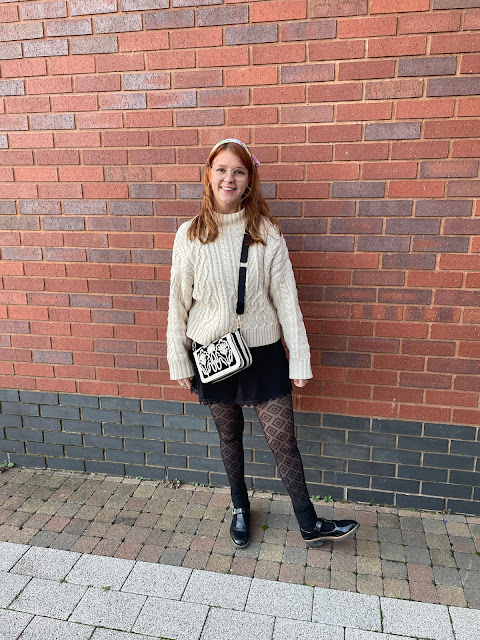 Writer and blogger Chloe Harriets outfit photo against brick wall. Knit jumper, patterned tights