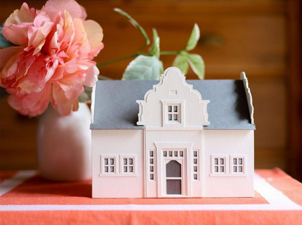 Cape Dutch white paper farmhouse displayed on peach and white cloth next to peony in white vase