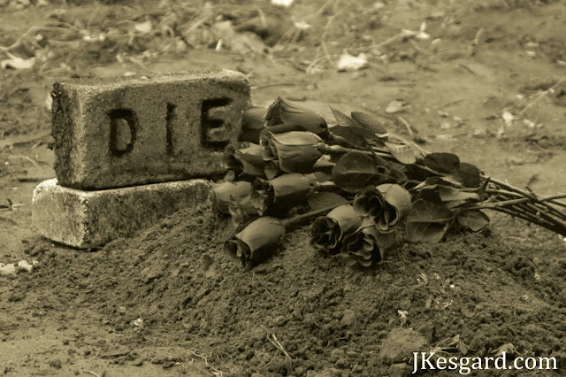 A gravesite with black roses and a headstone that says DIE