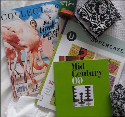 Selection of magazines on a bed, along with a number of black and white hankies and a bottle of  vitamin tablets.