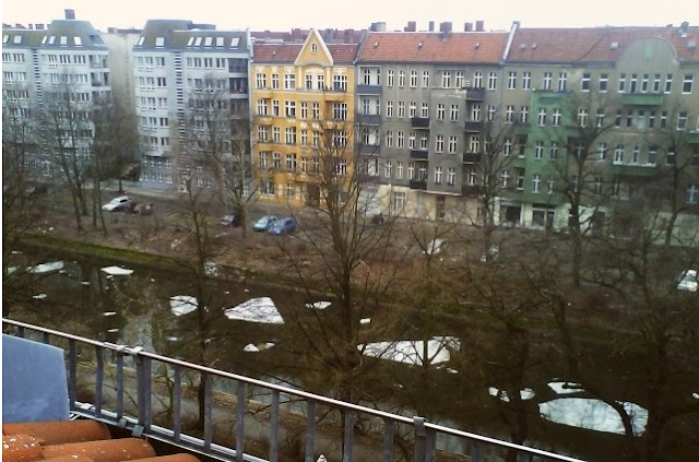 Von einer Dachetage aus fotografierte Häuserreihe, zu deren Füßen auf dem Kanal dicke, in Form und Größe unterschiedliche Schollen treiben.