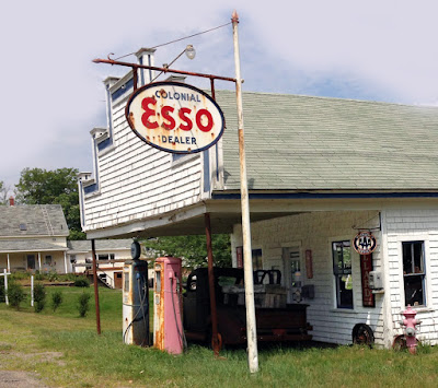 Exterior of old gasoline station, with old pumps and pickup truck.