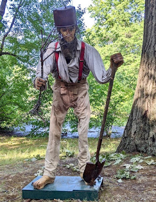 The figgure of Johnny Appleseed, holding a shovel and a sapling, and wearing old clothing and a pot for a hat