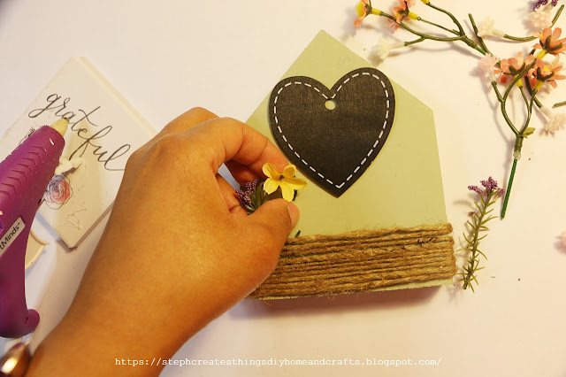 Hand placing flowers behind twine on wooden house plaque