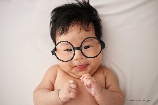 Bebe asiático com óculos e mostrando a língua