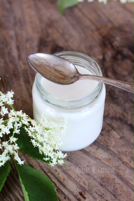 alt="yaourt blanc à la fleur de sureau sur une planche en bois décoré de fleur de sureau"