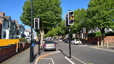 Cycle traffic lights with the cycle track bending across the road from left to right.