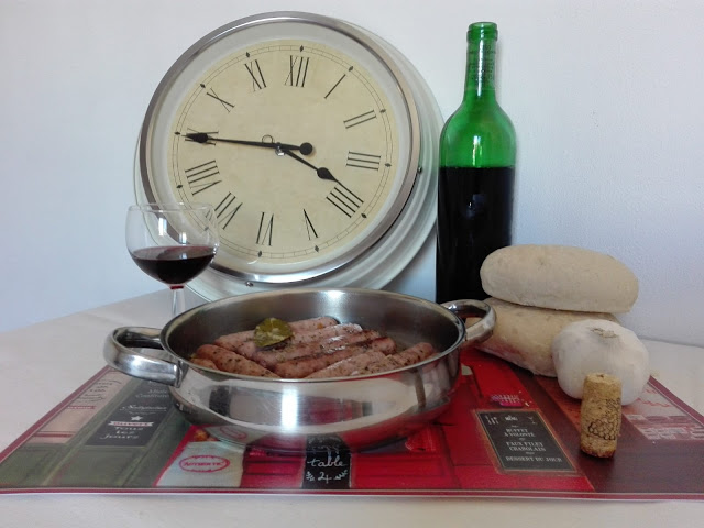 En la imagen tenemos las salchichas al vino blanco junto con pan de bollo antequerano y una copa con vino tinto