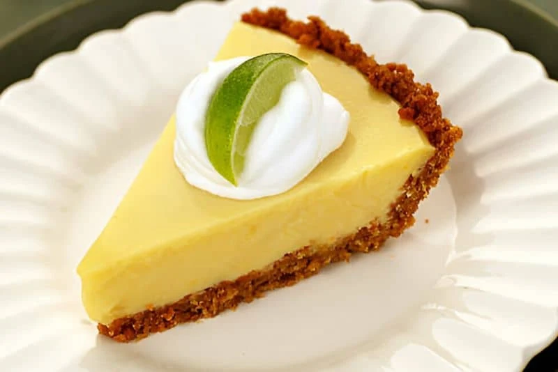 Un trozo de tarta Key Lime Pie adornada con crema chantilly y lima