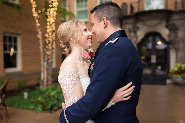 Shea & Tyler met while she was in grad school at Oklahoma State University in Stillwater, and he was in pilot training at Vance Air Force base in Enid.  His roommate, who just happened to be Shea’s best friend’s boyfriend, invited him on a weekend trip to Stillwater.  The stars were aligned, because every weekend after their first date that they were in the same state, they have spent together, and we are delighted to be celebrating their wedding day.    An intimate group of friends and family surrounded Shea and Tyler as they exchanged vows in the Heritage Room at the Ambassador Hotel located in the Midtown district of Oklahoma City.  The private, top-story, floor to ceiling windowed room provided a breathtaking view of the City.       The bride was breathtaking in her classic, A-line wedding gown from Simply Elegant Dress Boutique.  Shea’s jaw-dropping Stella York satin-chiffon wedding gown featured a scalloped lace train with a nude illusion back and buttons from neck to hip.  Her dynamic floral bouquet was courtesy of the talented Howard Brothers Florist, and Amy Cakes provided the elegantly decorated watercolor single tier wedding cake featuring two different flavors…strawberry and vanilla, while the mother of the bride made the groom a scrumptious chocolate cake!  Brushed Salon & Makeup Studio added the final, beautiful touches to this gorgeous bride.  Cheers to Shea & Tyler as they begin their married life in Clovis, New Mexico, with their newest family member, Frea, a Bluetick Coonhound!  