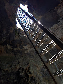 Underneath a metal stair ladder looking up to the top of the ladder at a cave opening