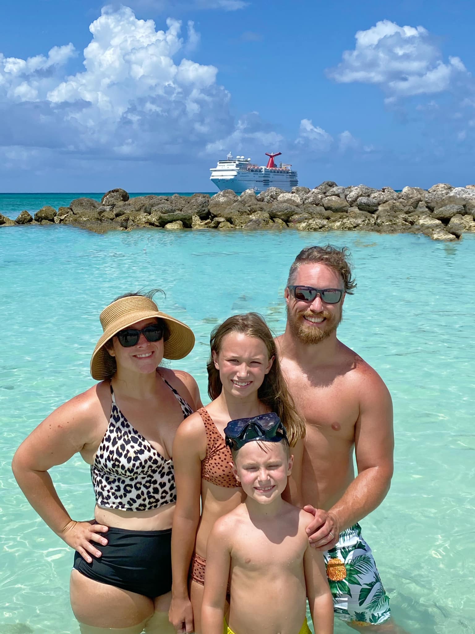 family of 4 in bathing suit at ocean in Bahamas. Carnival Cruise ship in background.