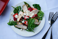 Plate of spinach salad with strawberries and grilled chicken.
