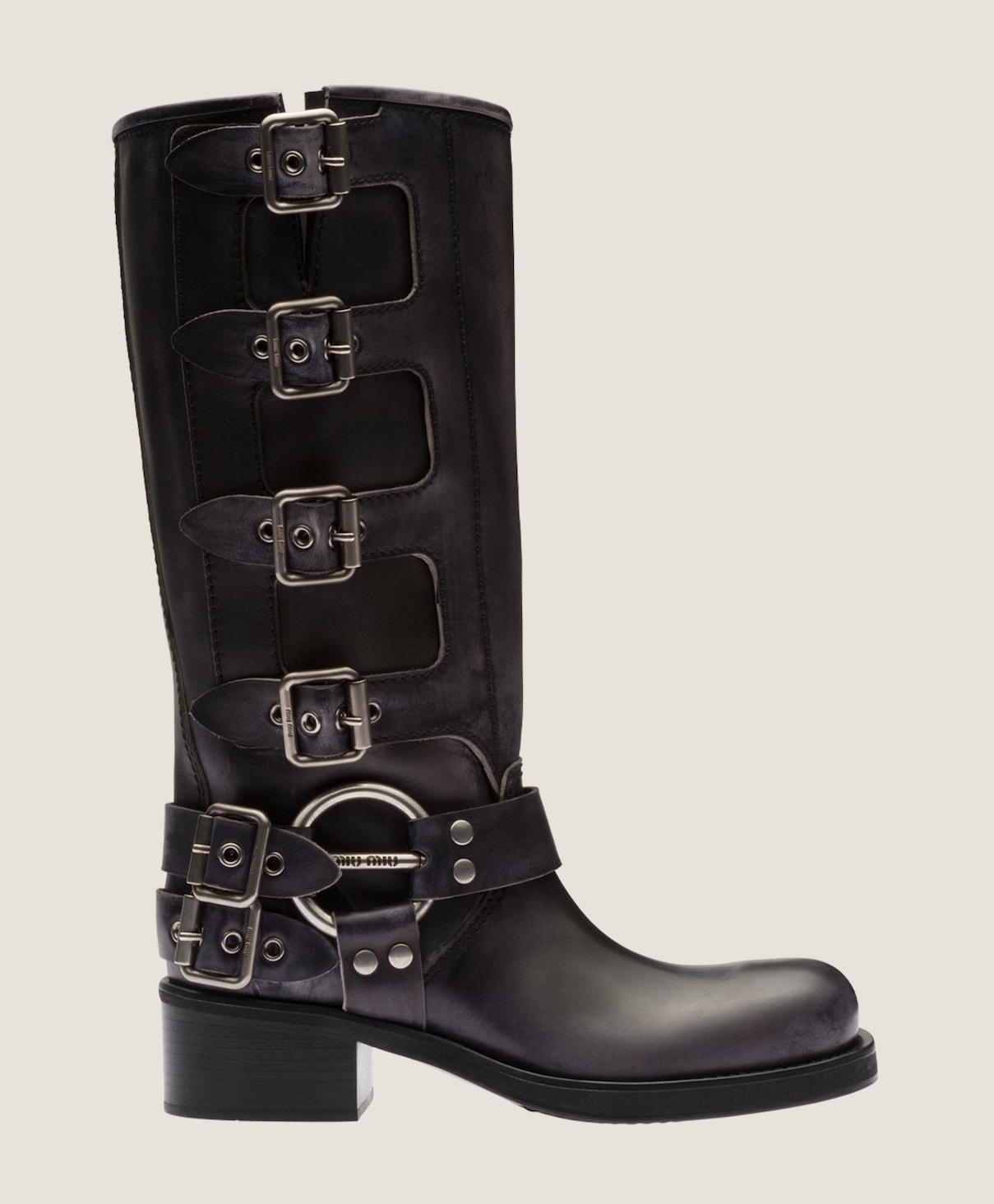 Black distressed leather tall moto biker boots with silver buckles, 1-inch black block heel and a silver buckle detail with Miu Miu logo on a beige backgroud