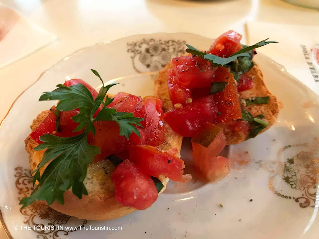 Tomato bruschetta decorated with parsley served on a white and gold porcelain plate.