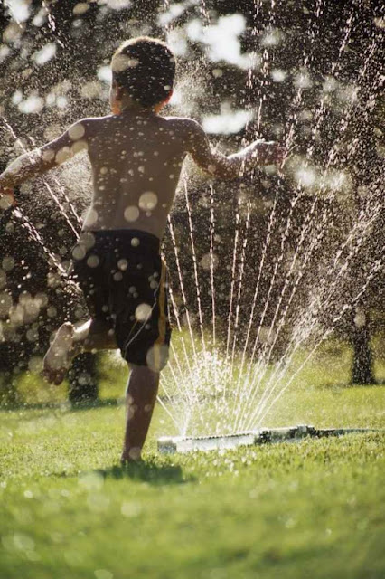طفل يجري فى نافورة الماء فى الحديقة هرباً من حرارة الشمس