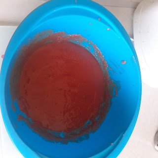 View from above into a large, blue, plastic bowl. In the bowl is a smooth, deep red soup.