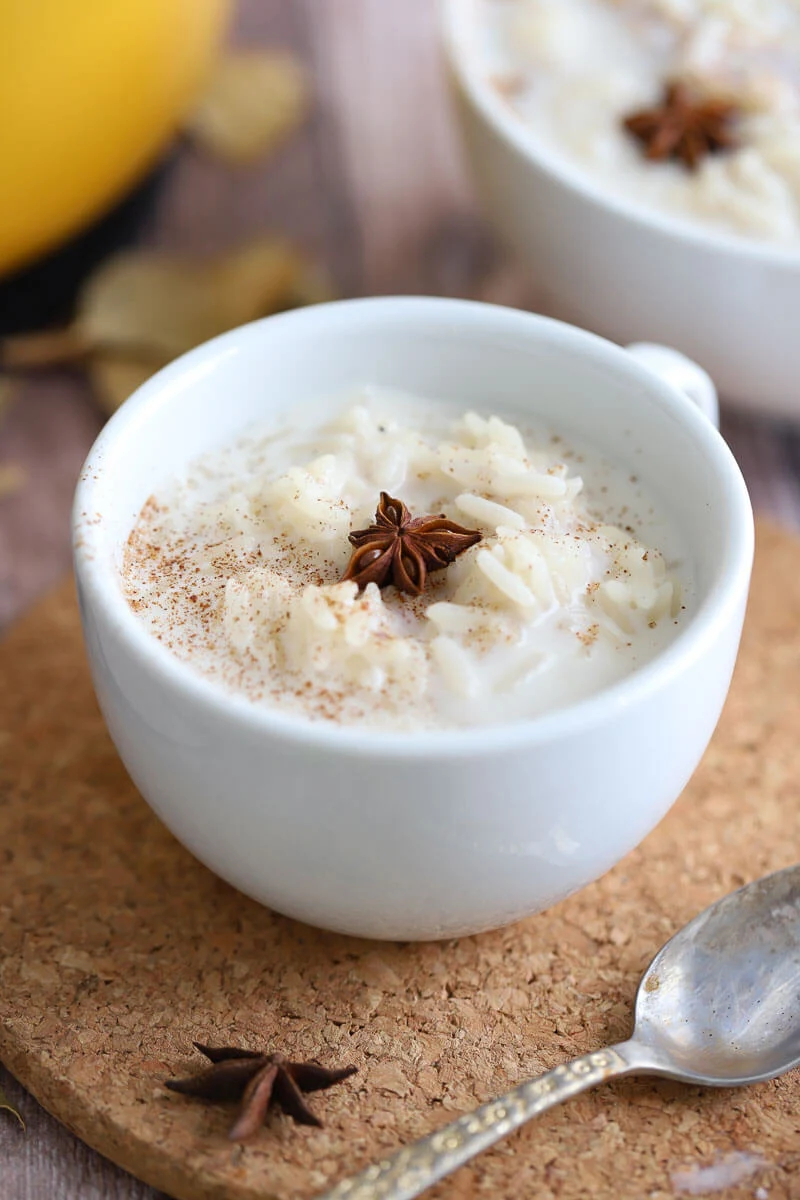 A small cup full of rice porridge on a brown coaster with aniseed in the middle and nutmeg sprinkled on top.