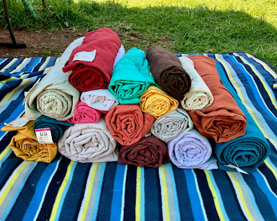 A pile of sheets have each been folded and rolled into a cylinder and stacked on top of each other. They are many different colours, including red, mustard yellow, chocolate brown, duck egg green, bright pink, and deep orange.