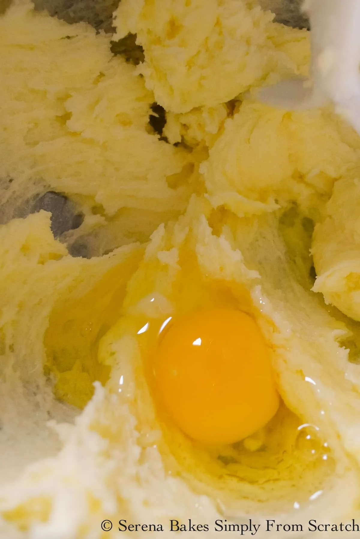 A whole egg added to creamed butter and sugar in a stainless steel mixing bowl.
