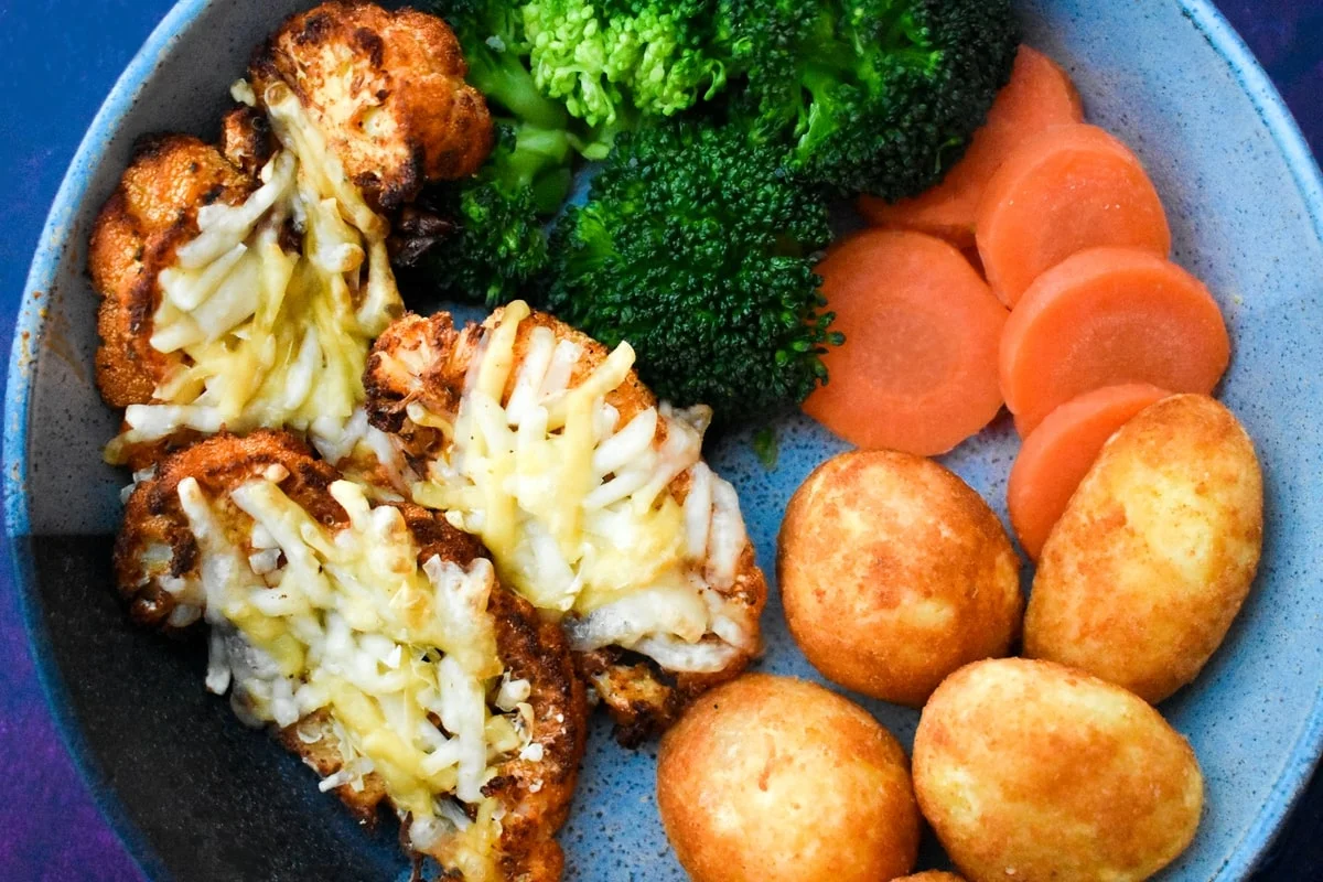 close up of cauliflower steaks served with veg.