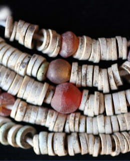 Beads found in a grave;  reddish-orange beads are carnelian, the faded-blue beads are faience, and the white are ostrich eggshell