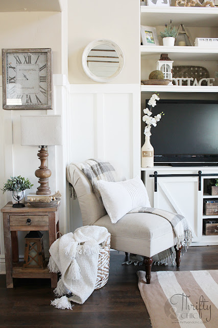 living room with white couch, large window, stacked wood, and shiplap mantel