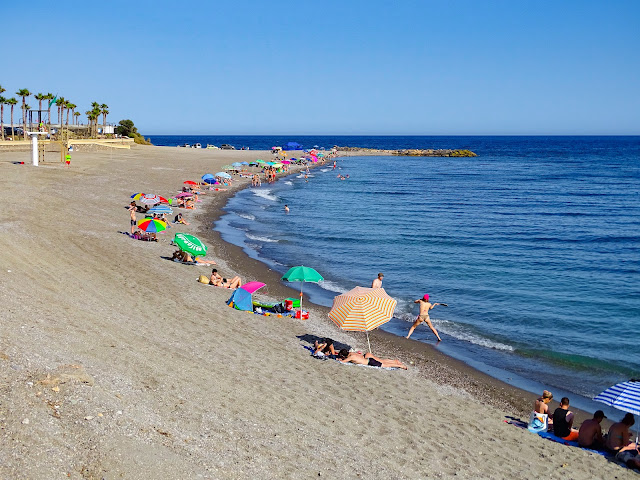 Playa de arena fina con sombrillas y turistas con el mar a su frente