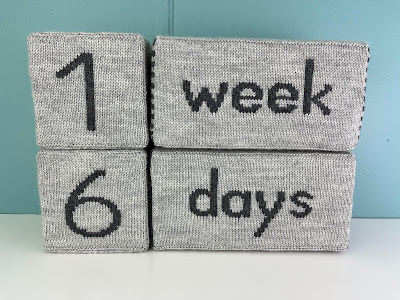 gray knitted milestone blocks sitting on a shelf showing 1 week 6 days