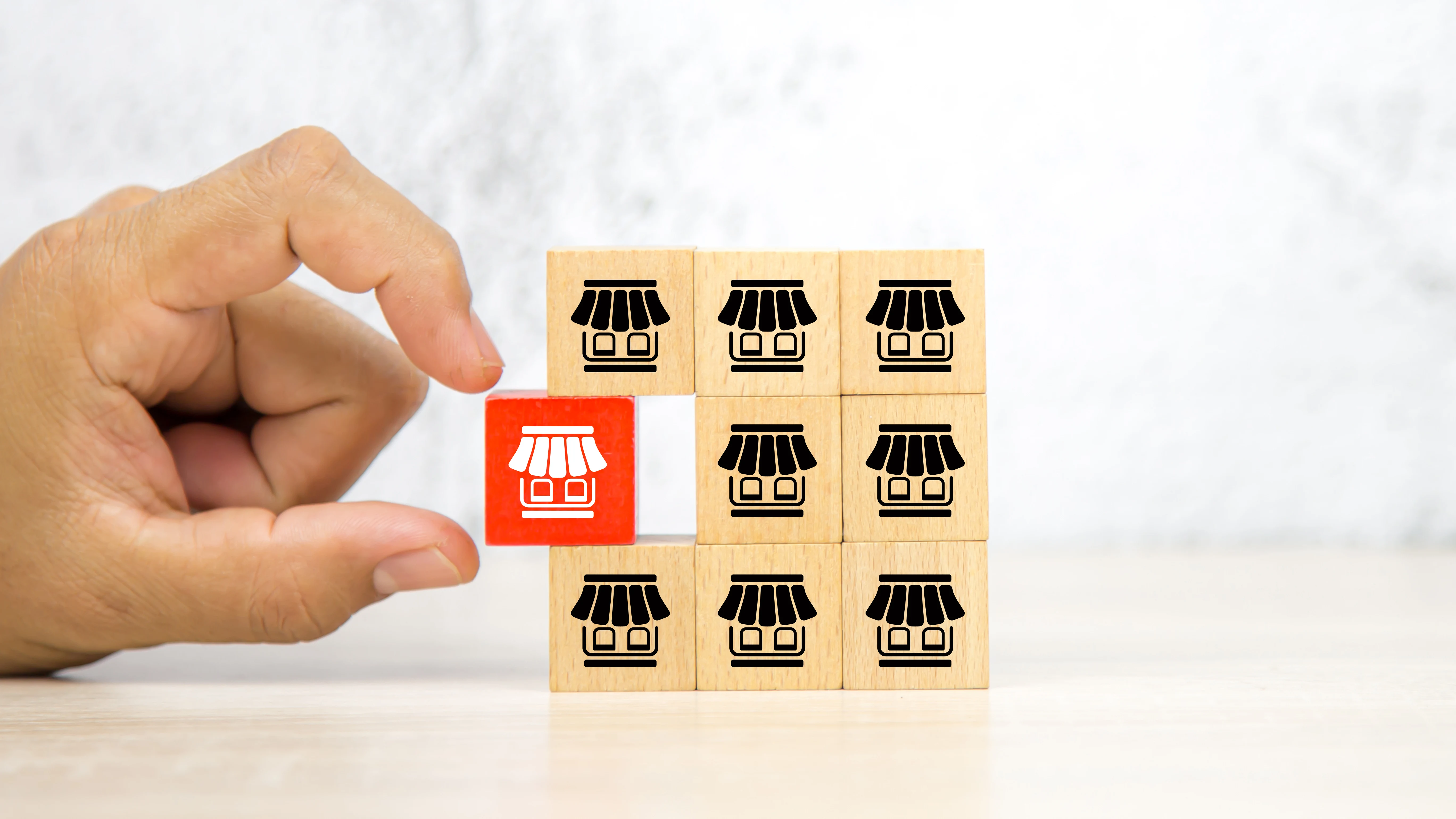 Mão de close-up escolhe pilha de blocos de madeira com ícone de loja de franquia para franquia para expansão de filial de crescimento e empréstimos bancários de negócios.