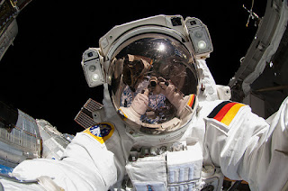 Alexander Gerst, astronauta da Nasa tira selfie no espaço.  Descrição: Foto com fundo escuro, Gerst de frente, na parte externa da estação espacial. Refletido no visor espelhado do capacete as mãos do próprio no instante da foto.