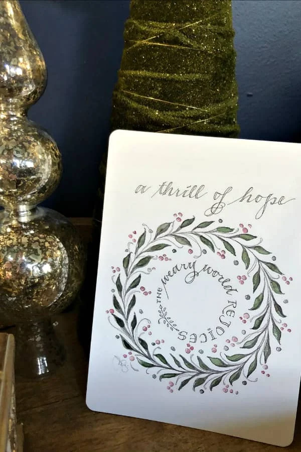 pen and ink wreath design Christmas card displayed next to ornament and tree