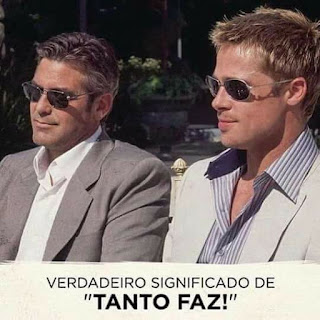 Foto ao ar livre em dia ensolarado de dois astros do cinema ​sentados lado a lado: à esquerda, George Clooney e à direita Brad Pitt, ambos com óculos escuros e discreto sorriso nos lábios. George é um homem de pele branca,  rosto oval, cabelos castanhos claros​ lisos​ com madeixas grisalhas, nariz afilado, lábios médios, bigode e barba por fazer; usa um paletó cinza sobre camisa branca. Brad é um homem de pele clara, rosto oval, cabelos ​lisos ​louros com luzes douradas, nariz levemente arrebitado, lábios médios, bigode e barba por fazer; usa um paletó gelo sobre camisa listrada em branco e azul. Abaixo em letras maiúsculas pretas e entre aspas em negrito, lê-se:  Verdadeiro significado de “TANTO FAZ!”