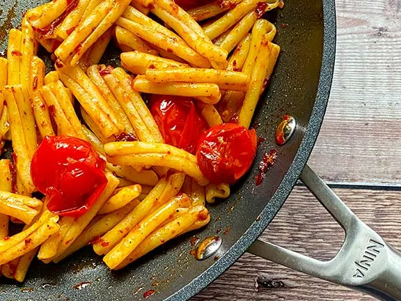 Pasta in a pan with tomatoes and harissa paste.